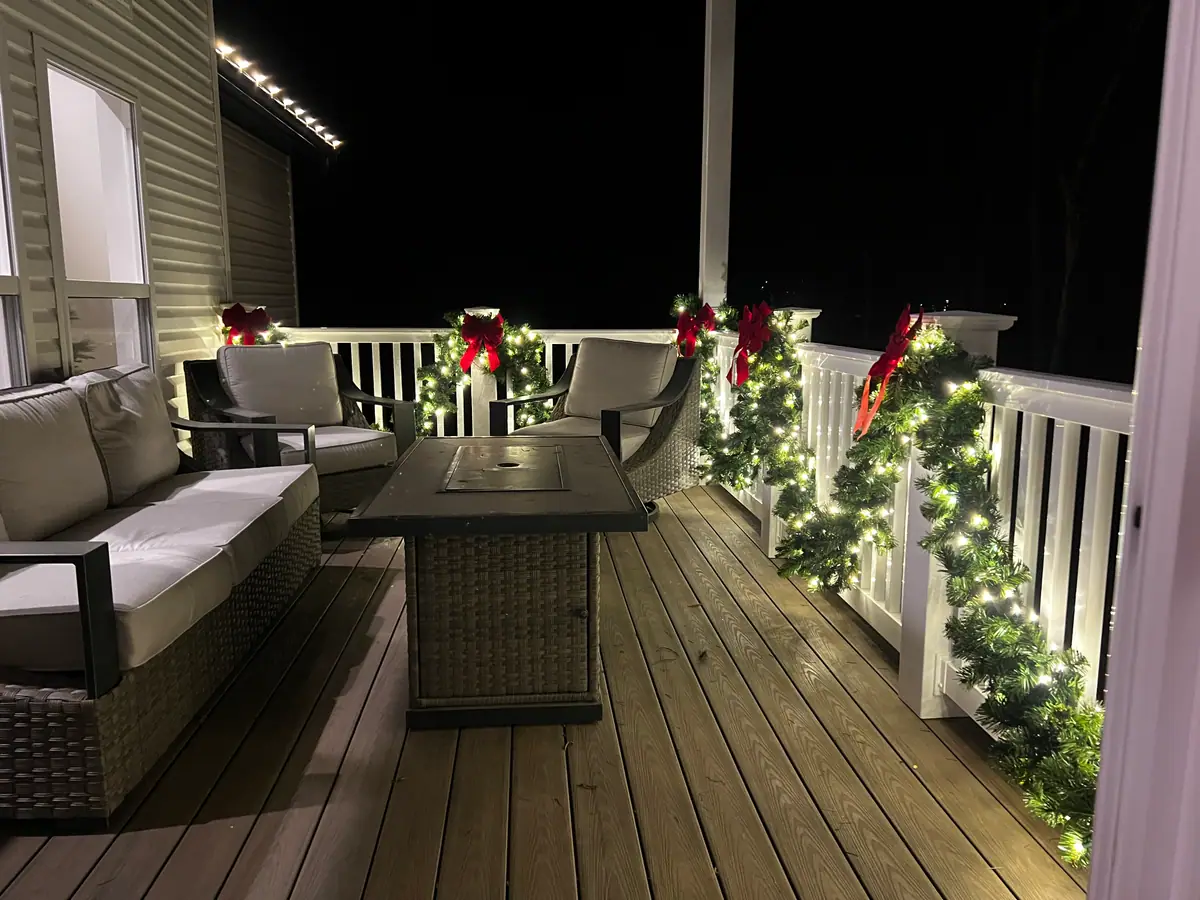 A covered porch railing wrapped in lit evergreen garland with deep red bows