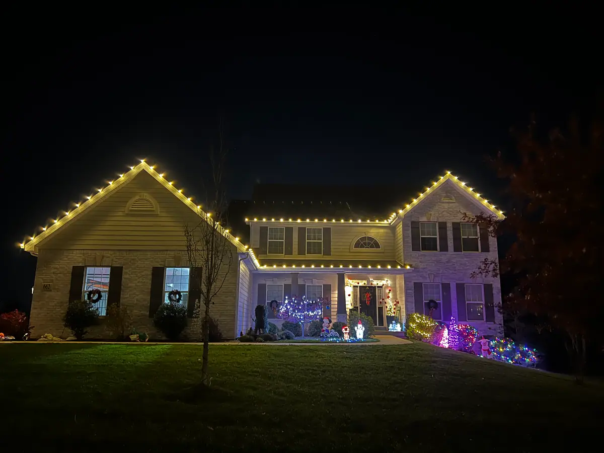 A two-story home with a warm white roofline and colored accent lighting washing the yard
